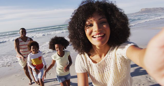Family having joyful time on the beach, mother capturing the moment with a selfie. Suitable for family vacation concepts, summer holiday themes, outdoor fun stories, advertisements about travel, and leisure activities.