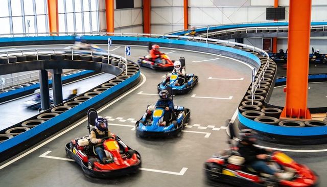 Go-kart drivers racing on multilevel banked indoor circuit with stacked tire barriers