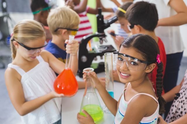 Children at school conducting science experiments in a laboratory, holding colorful beakers and wearing safety goggles. Ideal for educational content, STEM programs, school promotions, science-related articles, and children's educational materials.