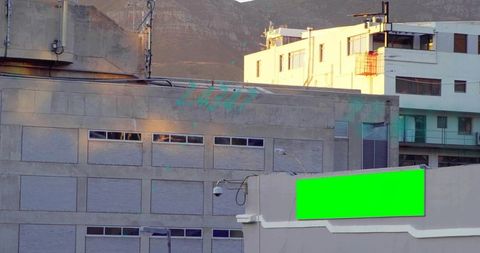 Urban industrial concrete facade with green billboard and surveillance camera at foothills