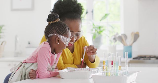 Mother and daughter engaging in a science experiment. Both wearing safety glasses, experimenting with test tubes in a kitchen. Camera capturing joyful expressions, highlighting intimate bond and enthusiasm for learning. Suitable for illustrating educational activities, family time, and scientific curiosity.