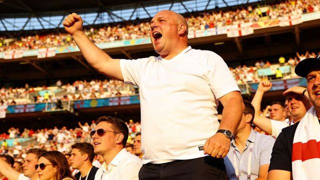 Sunlit bald fan cheering and raising fist in crowded stadium during lively football match