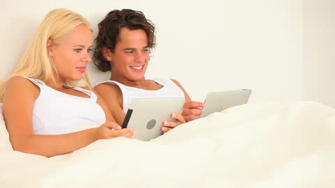 Happy Couple Relaxing with Tablets in Bed