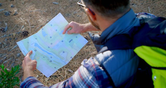 Caucasian man examines a map outdoors. He's navigating the terrain during a hiking adventure in nature.