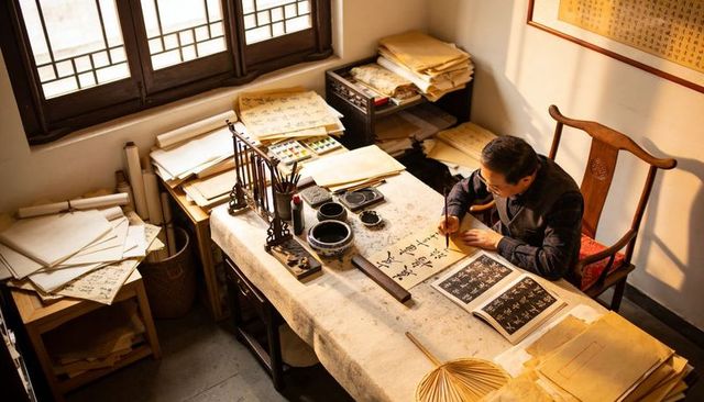 Calligrapher practicing chinese brush writing at traditional wooden desk with inkstones