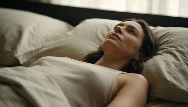 Woman lying on bed gazing upward in soft morning light for quiet contemplation