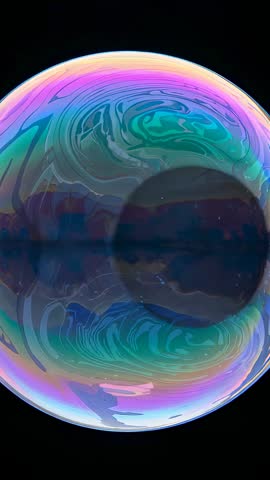 Vertical video iridescent soap bubble drifting, swirling rainbow colors over dark core