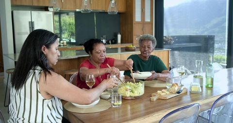 Women sharing salad and wine around modern kitchen table during casual home gathering