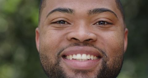 Smiling african american man with nose stud and beard outdoor portrait, bright bokeh