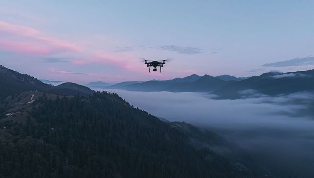 Hovering drone surveying fog-filled mountain valley at pink dawn over forested ridge