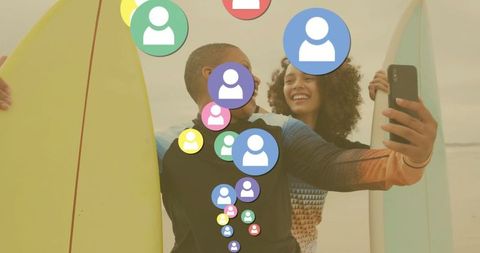 Friends taking sunset selfie on beach with surfboards