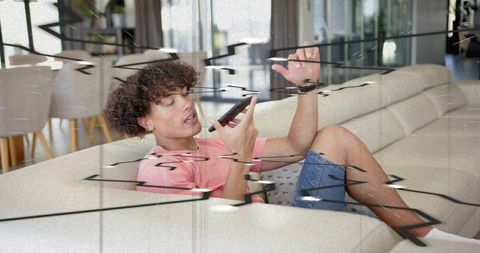 Young man relaxing on sofa using smartphone and sending voice message with glitch overlay