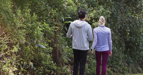Couple walking narrow woodland trail surrounded by dense vines and greenery, outdoor stroll