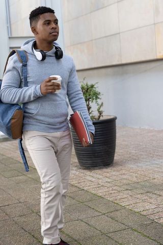 African american college student walking with coffee and backpack on urban campus