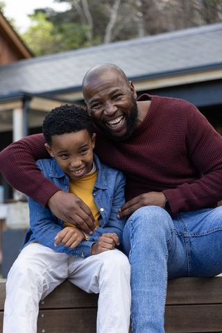 African american father laughing with son on porch bench sharing warm family bond