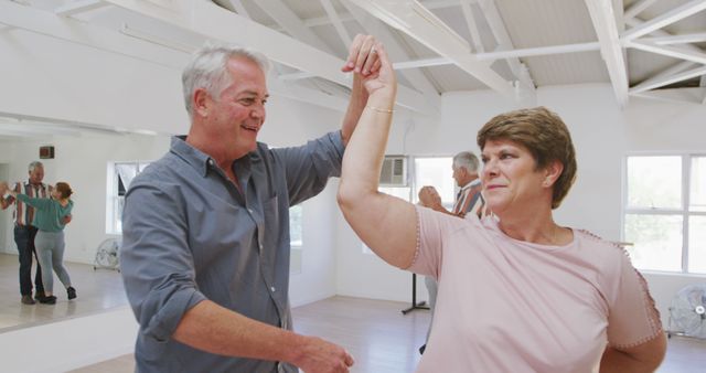 Senior couple dancing in a well-lit studio, enjoying each other's company and staying active. Perfect for advertisements related to senior health, dance classes for elderly, active aging lifestyle, social activities for seniors, or articles promoting mental and physical wellness among older adults.
