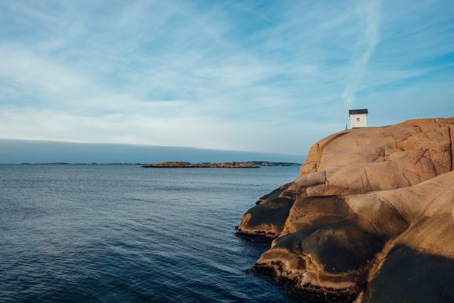 Majestic lighthouse standing on rugged rocky coastline with vast ocean and beautiful sky at sunrise. Perfect for use in travel brochures, nature magazines, desktop wallpapers, and marketing materials promoting coastal destinations or outdoor adventure experiences.