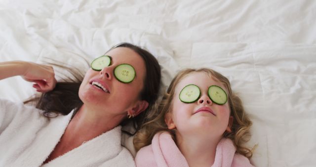 Caucasian mother and daughter having fun in bedroom. putting cucumber slices on their eyes. enjoying quality time at home during coronavirus covid 19 pandemic lockdown