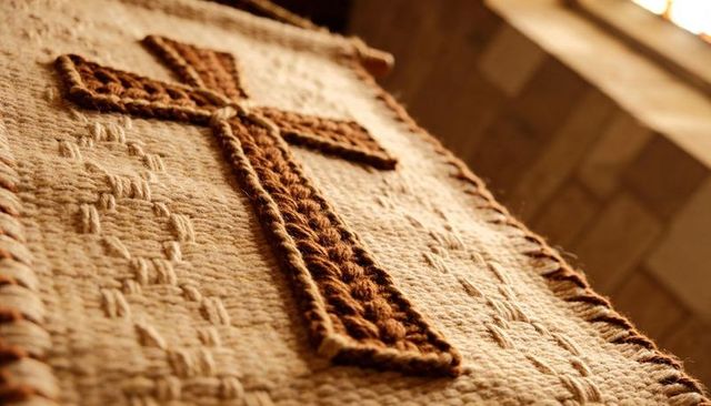 Handmade braided knitted cross resting on woven altar cloth in warm chapel light