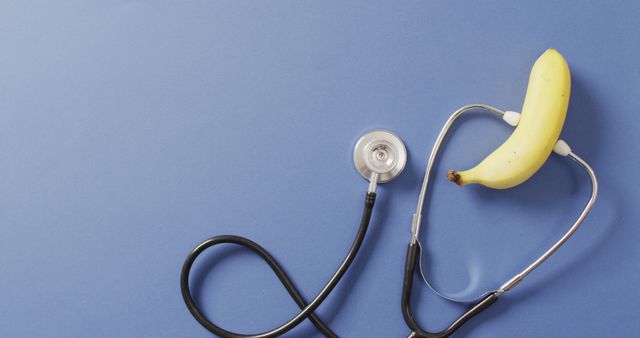 Creative presentation showing a stethoscope connected to a banana on a blue background, symbolizing the connection between nutrition and health. Useful for healthcare, wellness campaigns, diet initiatives, and creative health-related advertisements.