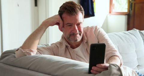 Senior Man Relaxing on Couch While Browsing Smartphone