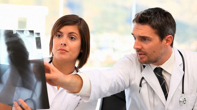 Medical professionals collaborating in hospital reviewing an x-ray scan for accurate patient diagnosis. Useful for topics related to healthcare teamwork, medical research, professional collaboration, and diagnostic procedures.