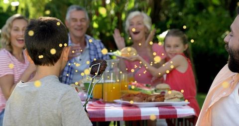 Boy offering grilled sausage at family backyard picnic celebrating three generations