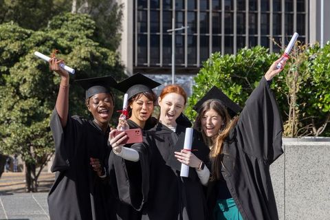 Multicultural female graduates taking selfie on campus quad celebrating diploma moment