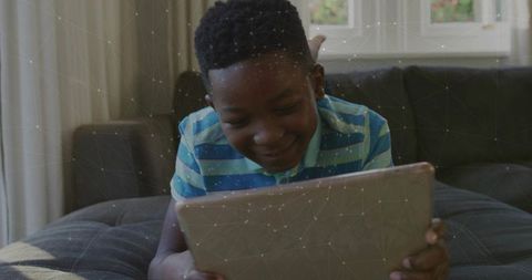 Young boy using tablet for online learning on sofa with digital network overlay