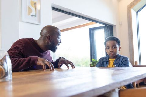 African american father expressing frustration while son sitting quietly at dining table