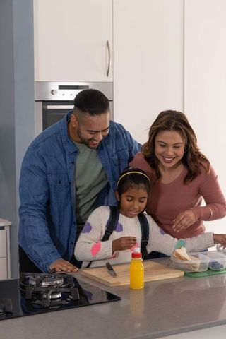 Parents helping daughter assemble school lunch at modern kitchen island