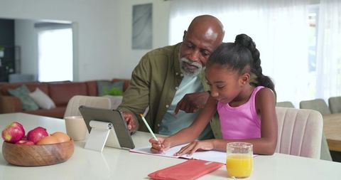 African american mature man helping girl with homework at sunlit kitchen table