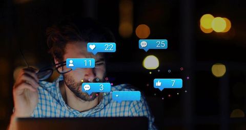 Man holding glasses working late on laptop with floating social media notification badges