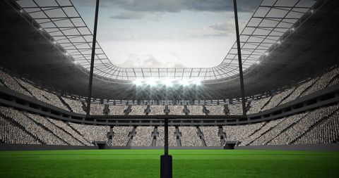 Empty Football Stadium with Illuminated Goalposts Under Cloudy Sky
