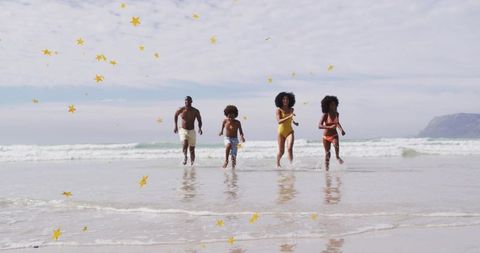 Family of four running and splashing on beach with yellow confetti and ocean reflections
