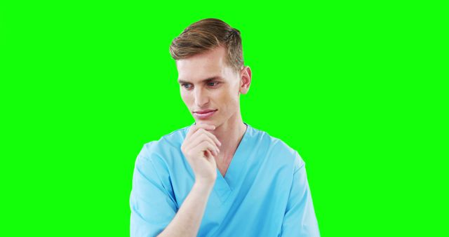 Young male nurse is contemplating while dressed in blue medical scrubs, isolated on a vibrant green screen background. Ideal for healthcare, medical training materials, advertisements, or creating custom backgrounds and graphics.