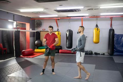 Two men sparring in mma gym wearing boxing gloves on matted floor with hanging heavy bags