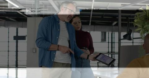 Colleague pointing at tablet with analytics while teammate reviewing data in open-plan office