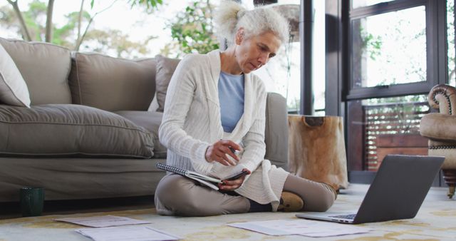 Senior biracial woman sitting on floor using laptop. retirement and senior lifestyle, spending time alone at home.