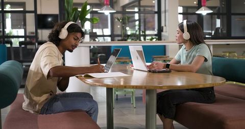 African American students studying with laptops and headphones in modern coworking hub
