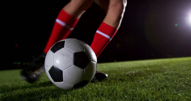 A soccer player is about to kick a ball during a night game, with copy space. Capturing the action and intensity of a soccer match, the focus is on the player's feet and the iconic black and white ball.