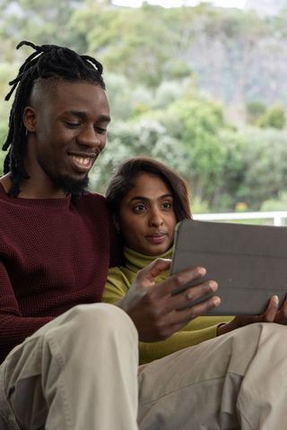 African american man and asian woman relaxing on porch using tablet together