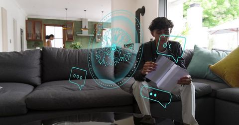 Young man flipping documents on sofa with holographic ai chat overlays in modern living room