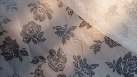 Cream floral fabric bedspread catching warm sunlight with sheer curtain overlay