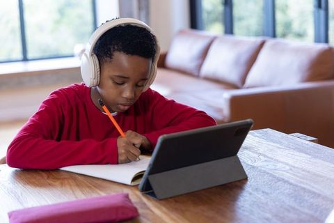 African american boy studying with tablet and headphones at home remote learning setup