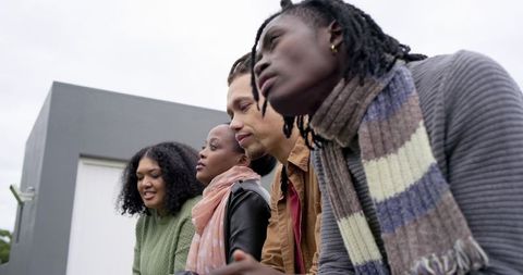 Multiracial friends leaning on rooftop railing observing urban view