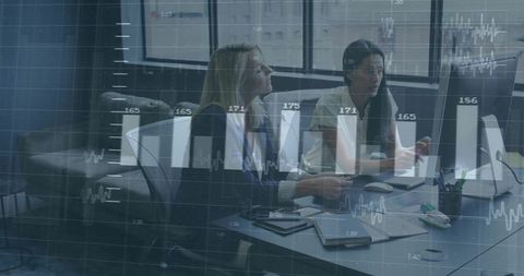 Two Women Executives Discussing Financial Charts and Business Analytics on Desktop Screens
