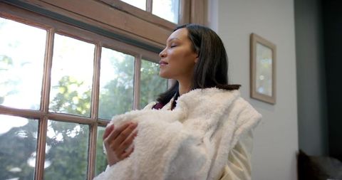 Mother Cradling Infant in Cozy Home by Sunlit Window