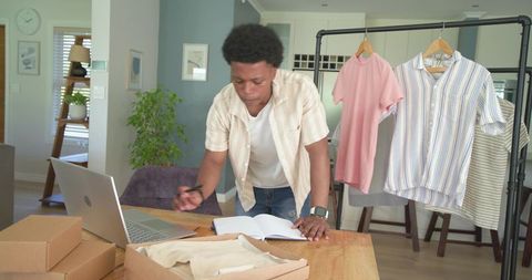 African american entrepreneur packing clothing orders in home office workstation