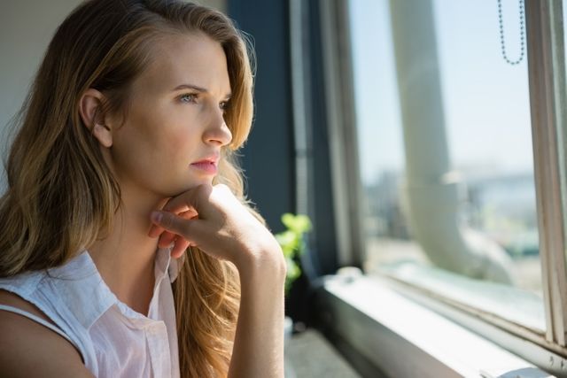 Young thoughtful businesswoman looking through window at office